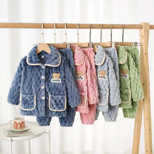 Children's Pajamas Autumn Flannel Home in light blue, pink, green hanging on a rack with cute teddy bear design.